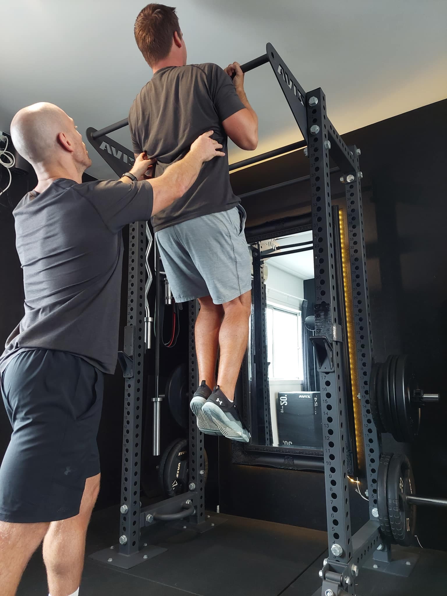 A photo of Coach Ryan assisting a client doing pull-ups